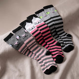 Four pairs of crew socks arranged on a beige fabric surface. The socks feature cat-themed designs with black, gray, pink, white, and light blue colors, including stripes, solid sections, and cartoon cat face details.