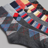 Four pairs of men's dress socks arranged diagonally, featuring argyle and striped patterns in various colorways including gray, navy, red, blue, orange, and cream.