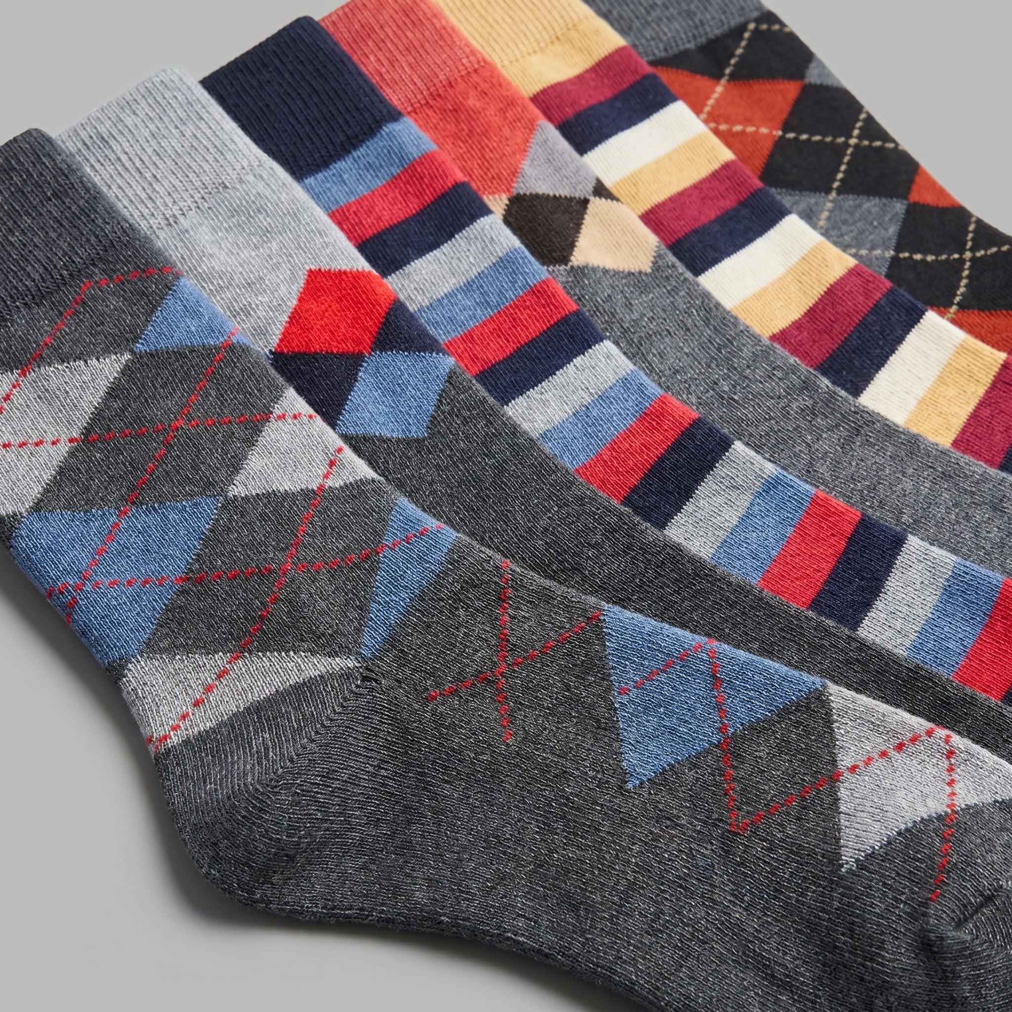 Four pairs of men's dress socks arranged diagonally, featuring argyle and striped patterns in various colorways including gray, navy, red, blue, orange, and cream.