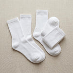 Four pairs of plain white crew socks arranged on a light beige textured fabric background.