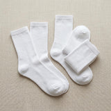 Four pairs of plain white crew socks arranged on a light beige textured fabric background.