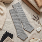 Gray knee-high socks on a textured surface with a mug labeled 'COZY' and lavender flowers.