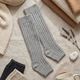 Gray knee-high socks on a textured surface with a mug labeled 'COZY' and lavender flowers.