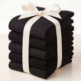 A stack of folded black ribbed knit socks or hosiery tied with a cream ribbon bow, photographed on a light neutral background.
