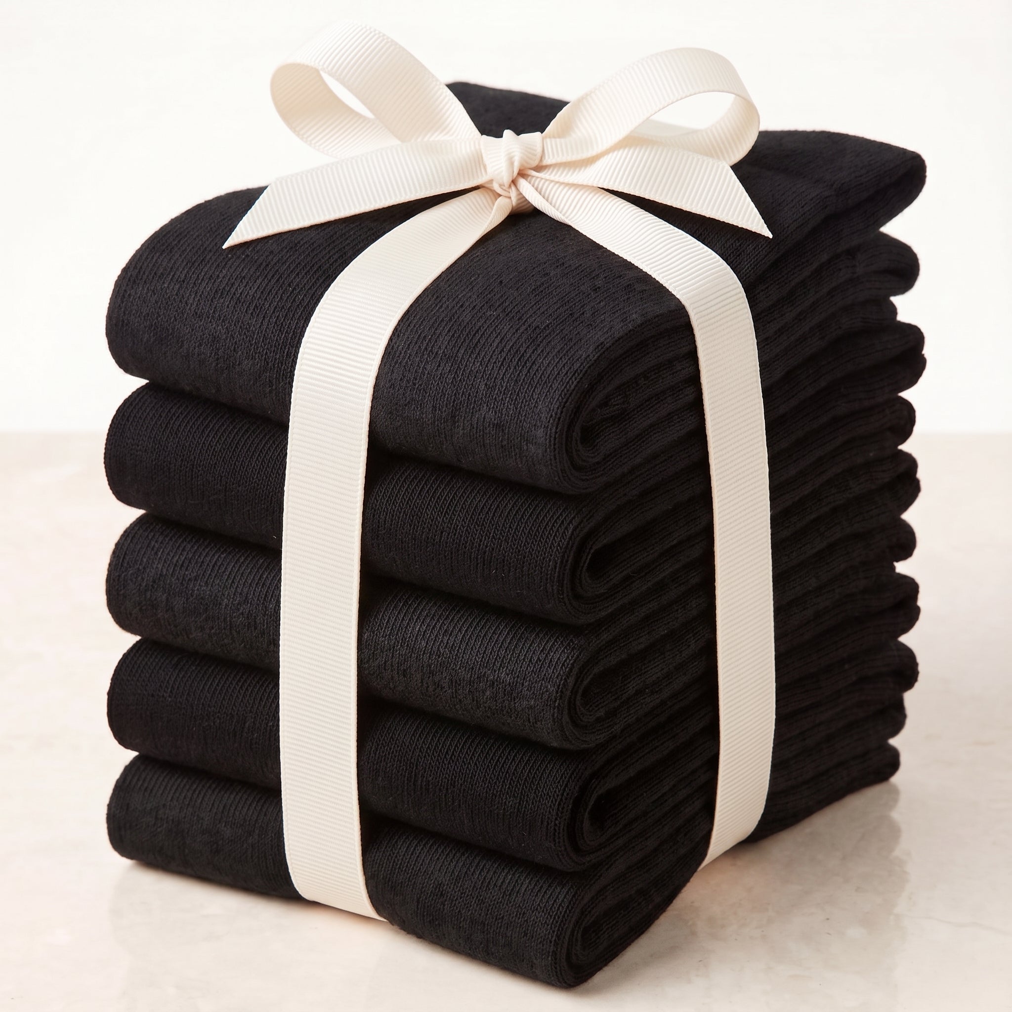 A stack of folded black ribbed knit socks or hosiery tied with a cream ribbon bow, photographed on a light neutral background.