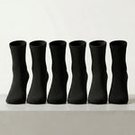 Six black crew socks arranged in a row on a light gray surface against a white background.