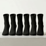 Six black crew socks arranged in a row on a light gray surface against a white background.