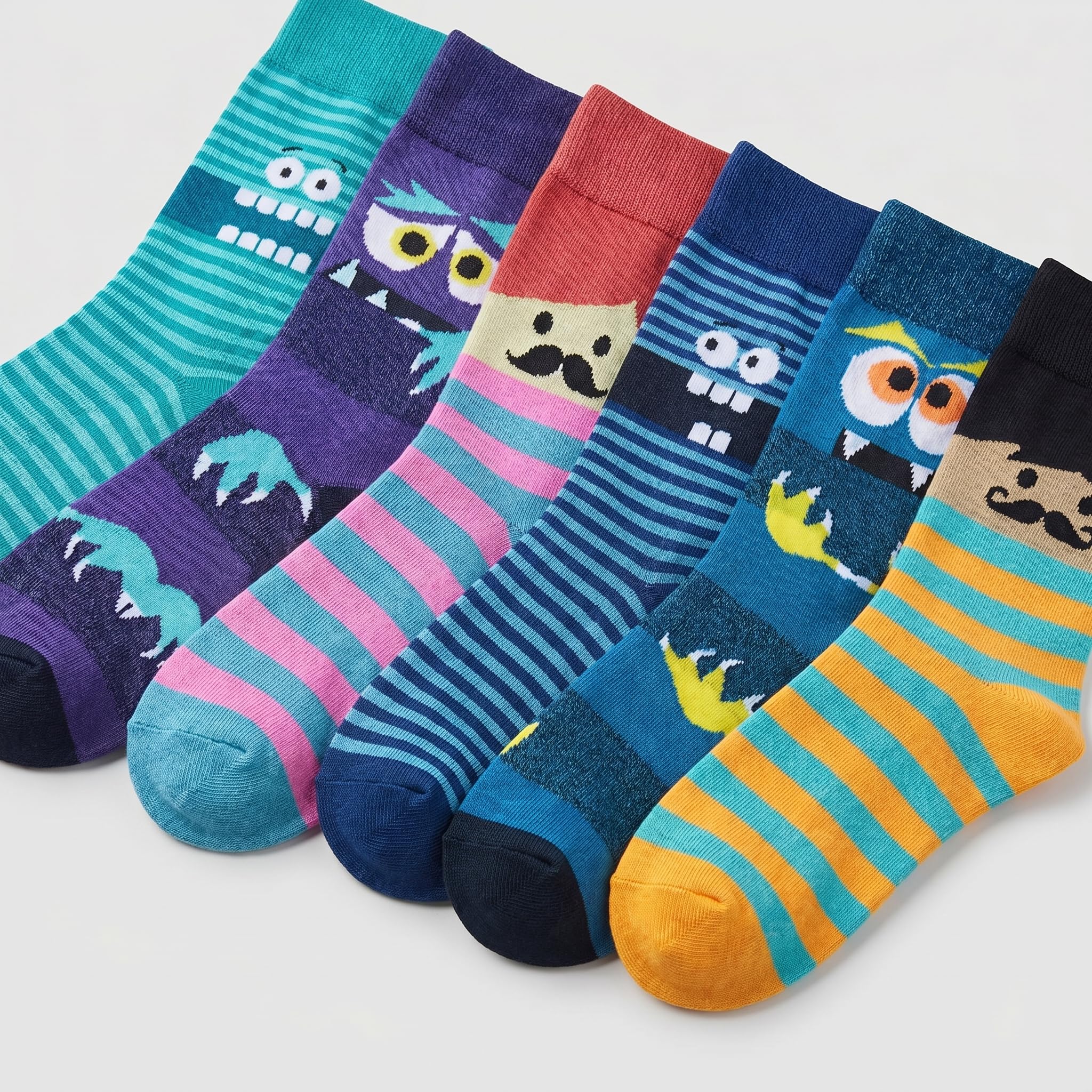 Six colorful children's socks arranged in a fan shape on a light gray background. Each sock features a different cartoon monster or character design with stripes and solid sections in teal, purple, pink, red, navy, blue, yellow, and orange.