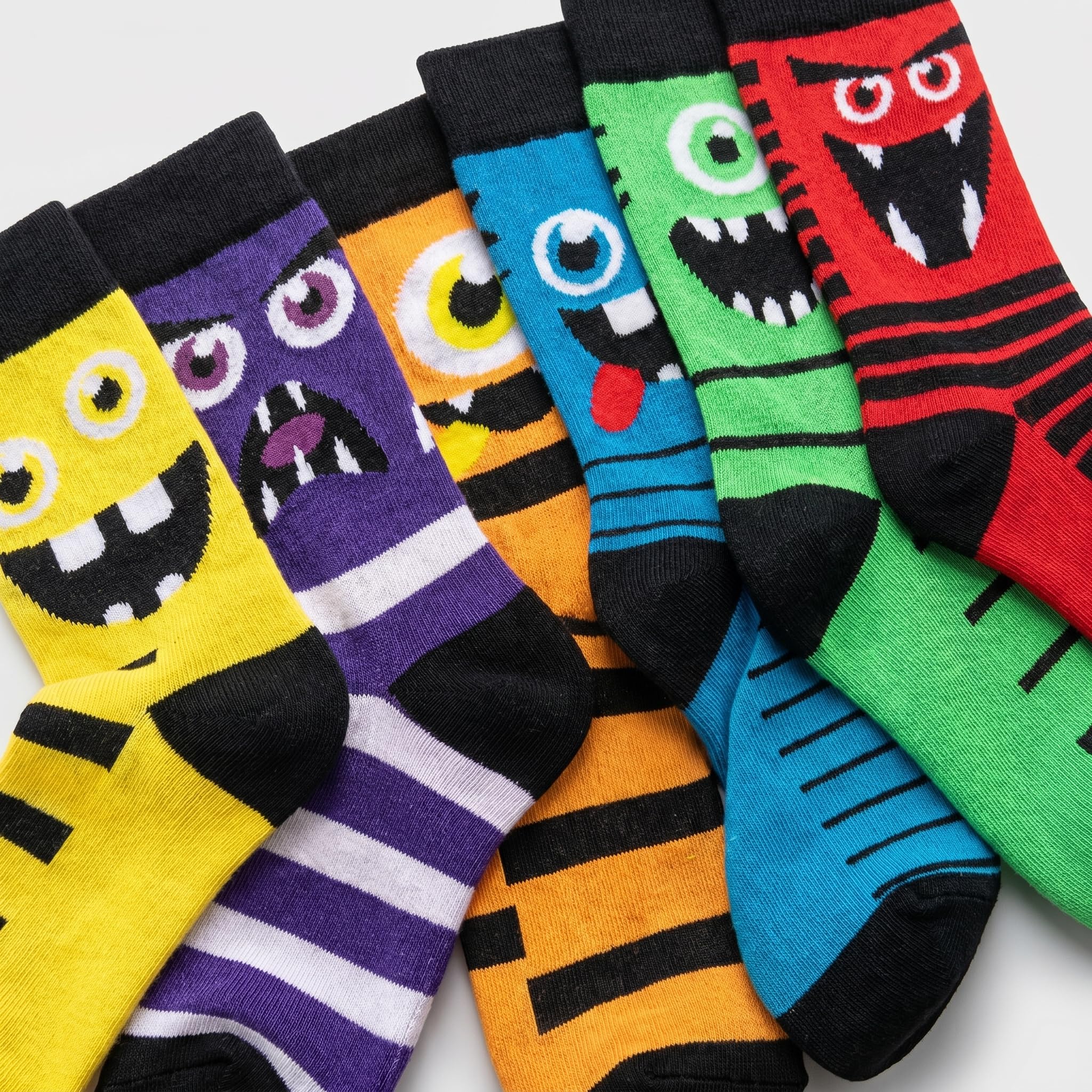 Six pairs of colorful monster-themed crew socks arranged in a fan shape on a light gray background. The socks feature bright colors including yellow, purple, orange, blue, green, and red, each with a unique cartoon monster face design and black accents.