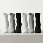 Six pairs of crew socks arranged in a row on a light surface against a white background, alternating between solid white, light gray, black, white, light gray, and black.