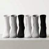 Six pairs of crew socks arranged in a row on a light surface against a white background, alternating between solid white, light gray, black, white, light gray, and black.
