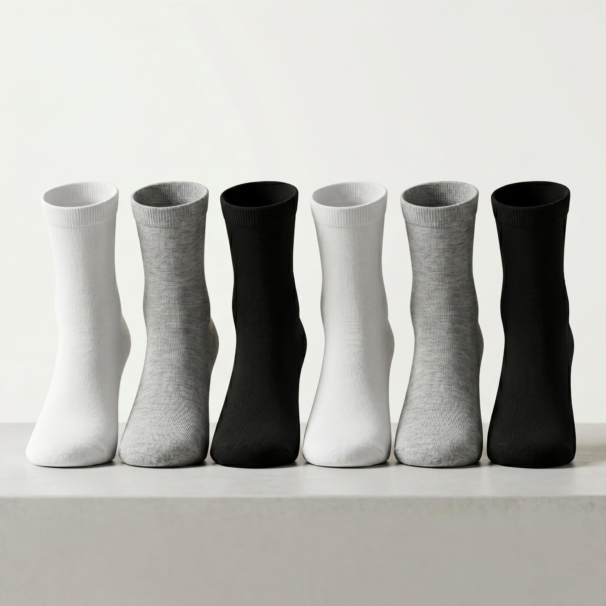 Six pairs of crew socks arranged in a row on a light surface against a white background, alternating between solid white, light gray, black, white, light gray, and black.