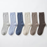 Six pairs of crew socks in different muted colors, arranged in a row on a plain white background. The colors are light gray, light blue, medium blue, cream, taupe, and dark brown.