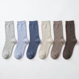 Six pairs of crew socks in different muted colors, arranged in a row on a plain white background. The colors are light gray, light blue, medium blue, cream, taupe, and dark brown.