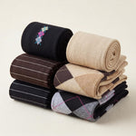 Six pairs of folded and rolled knit socks in various patterns and colors, including solid beige, black with colorful embroidery, brown with white stripes, and argyle designs, arranged on a light beige background.
