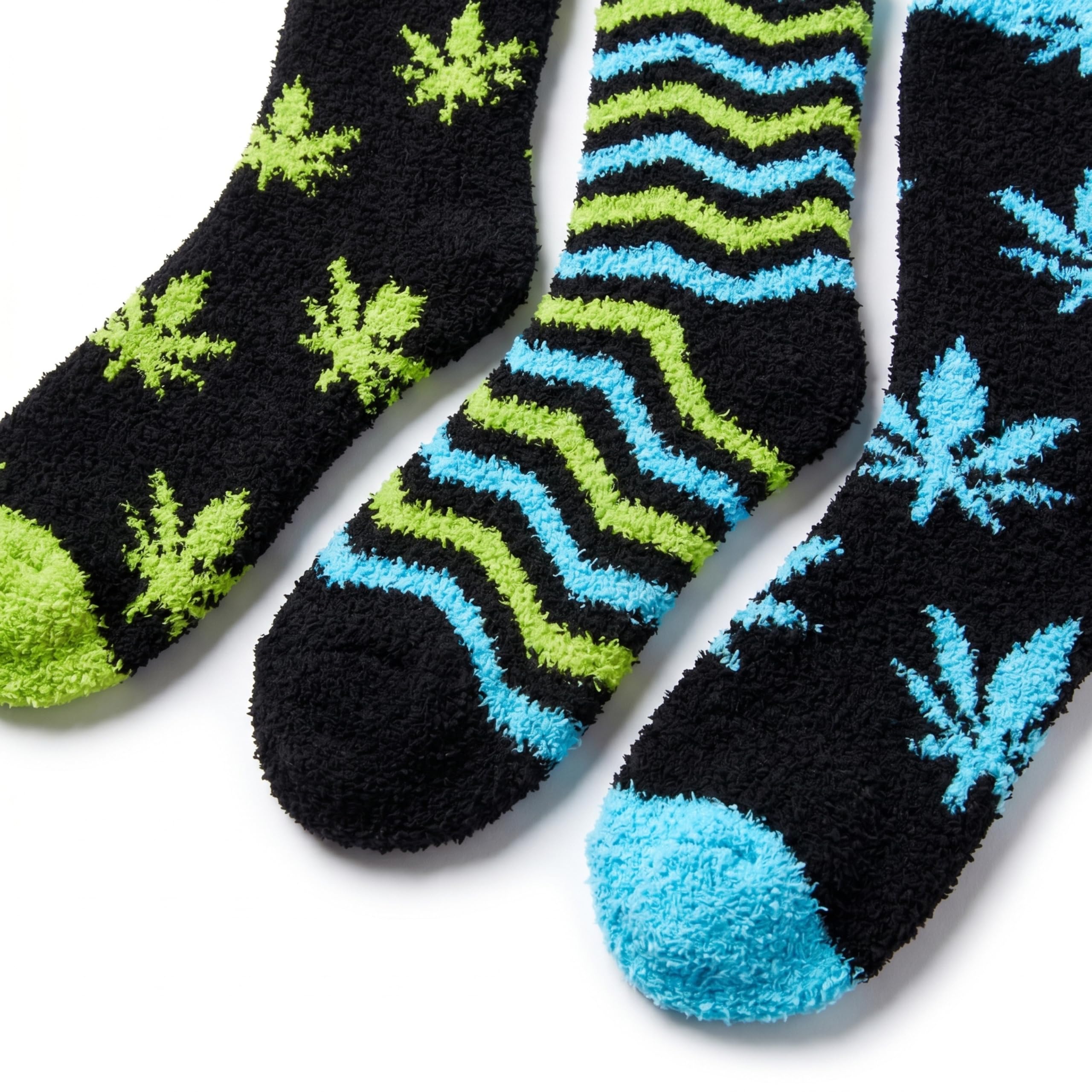 Three fuzzy socks laid diagonally on a white background. The left sock is black with bright green leaf motifs and a green toe.