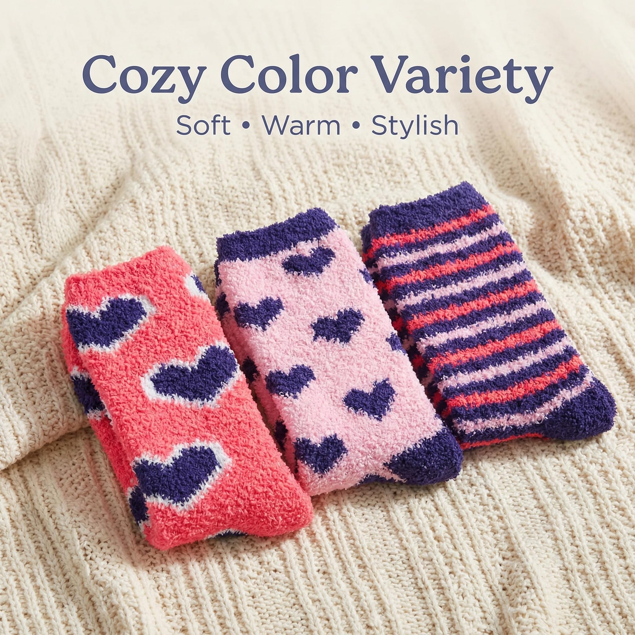 Three pairs of cozy fuzzy socks displayed on a cream-colored knit blanket, with text overlay reading 'Cozy Color Variety' and 'Soft • Warm • Stylish'. The socks feature different patterns: pink with dark purple hearts, light pink with dark purple hearts, and dark purple with coral-pink and white stripes.