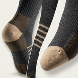 Three pairs of crew socks shown in a close-up studio arrangement on a light neutral background. The socks are dark charcoal gray with tan/beige toe, heel, and cuff sections, plus thin beige stripes on one pair.