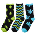 Three pairs of fuzzy crew socks on a plain white background. The left pair is black with lime green cannabis leaf patterns and green toe/heel accents.