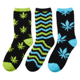 Three pairs of fuzzy crew socks on a plain white background. The left pair is black with lime green cannabis leaf patterns and green toe/heel accents.