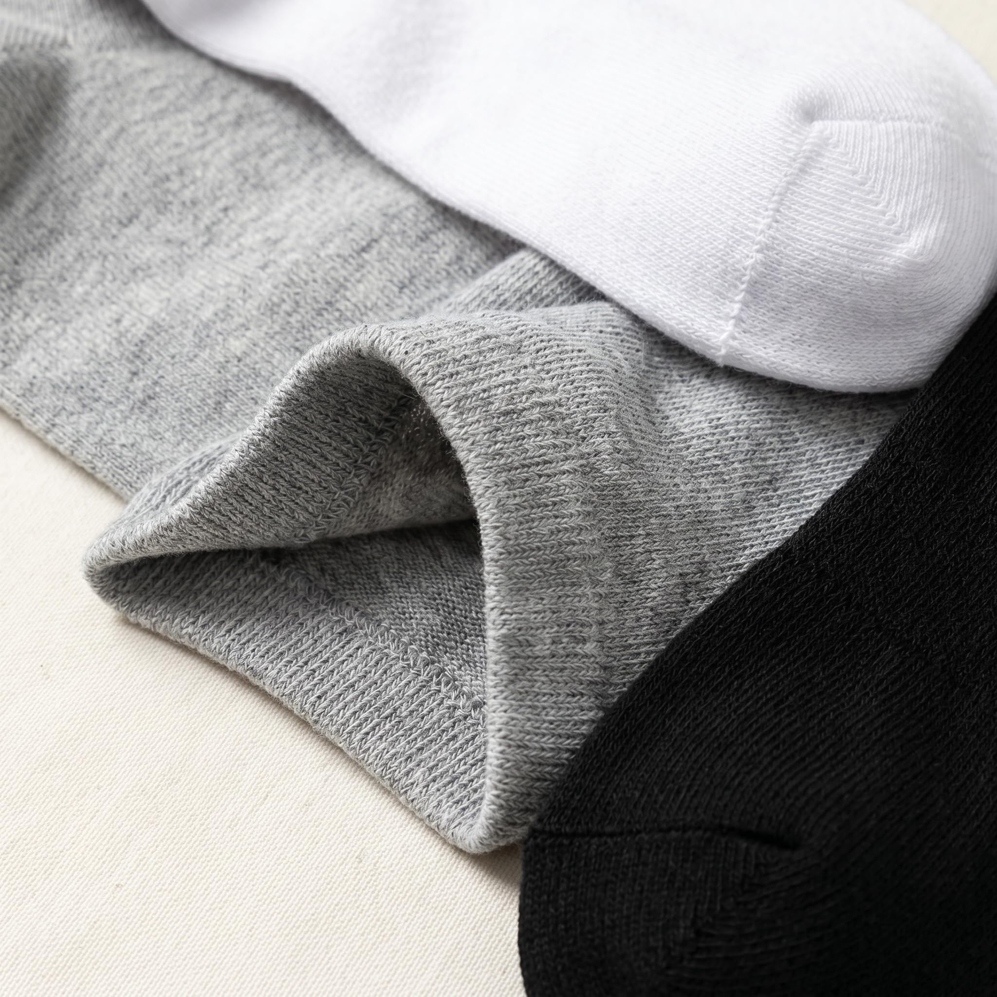 Three pairs of ribbed knit socks stacked diagonally, showing gray, white, and black colors with a close-up of the gray cuff texture.