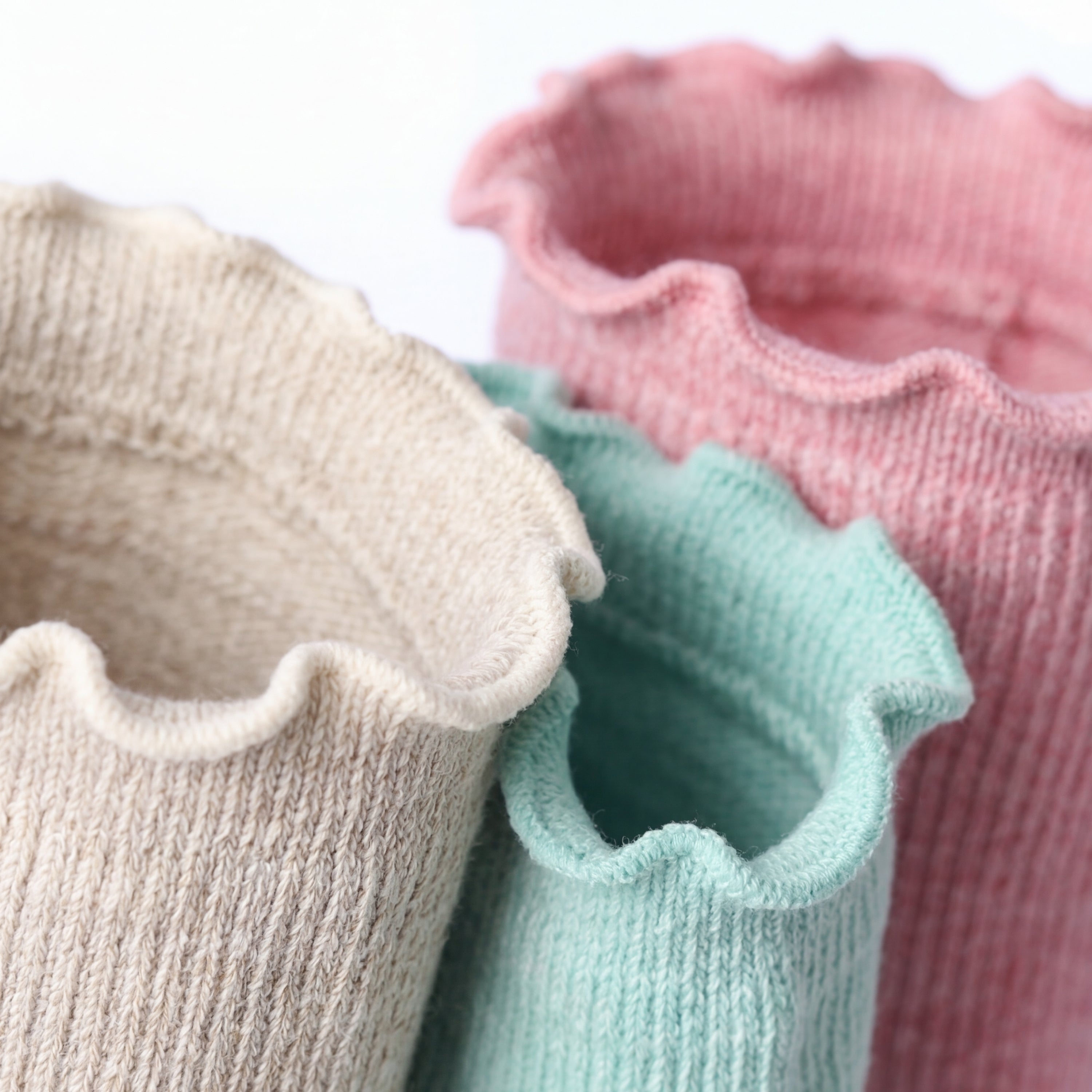 Three pairs of ruffled socks in beige, green, and pink on a white background