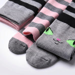 Three pairs of striped socks arranged on a white background. One pair is gray and pink with black stripes, another is pink and gray with black stripes, and the front pair is gray with a cute embroidered cat face in green, black, and pink.
