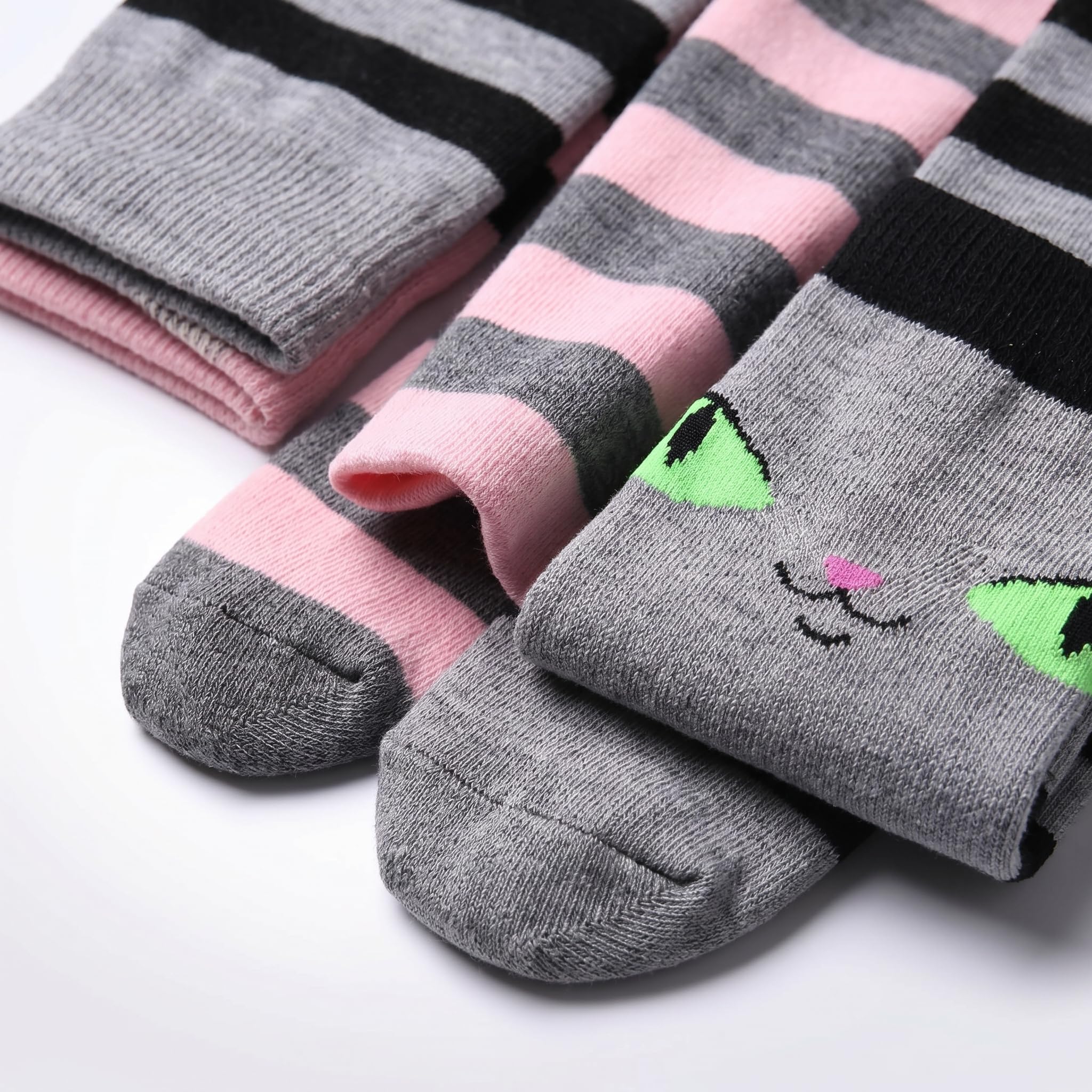 Three pairs of striped socks arranged on a white background. One pair is gray and pink with black stripes, another is pink and gray with black stripes, and the front pair is gray with a cute embroidered cat face in green, black, and pink.