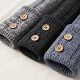 Three ribbed knit sleeve cuffs in heather gray, charcoal, and heather blue, each detailed with a single round wooden button, arranged diagonally on a textured off-white fabric background.