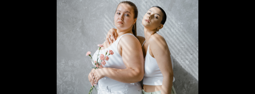 Two women standing close together against a gray wall.
