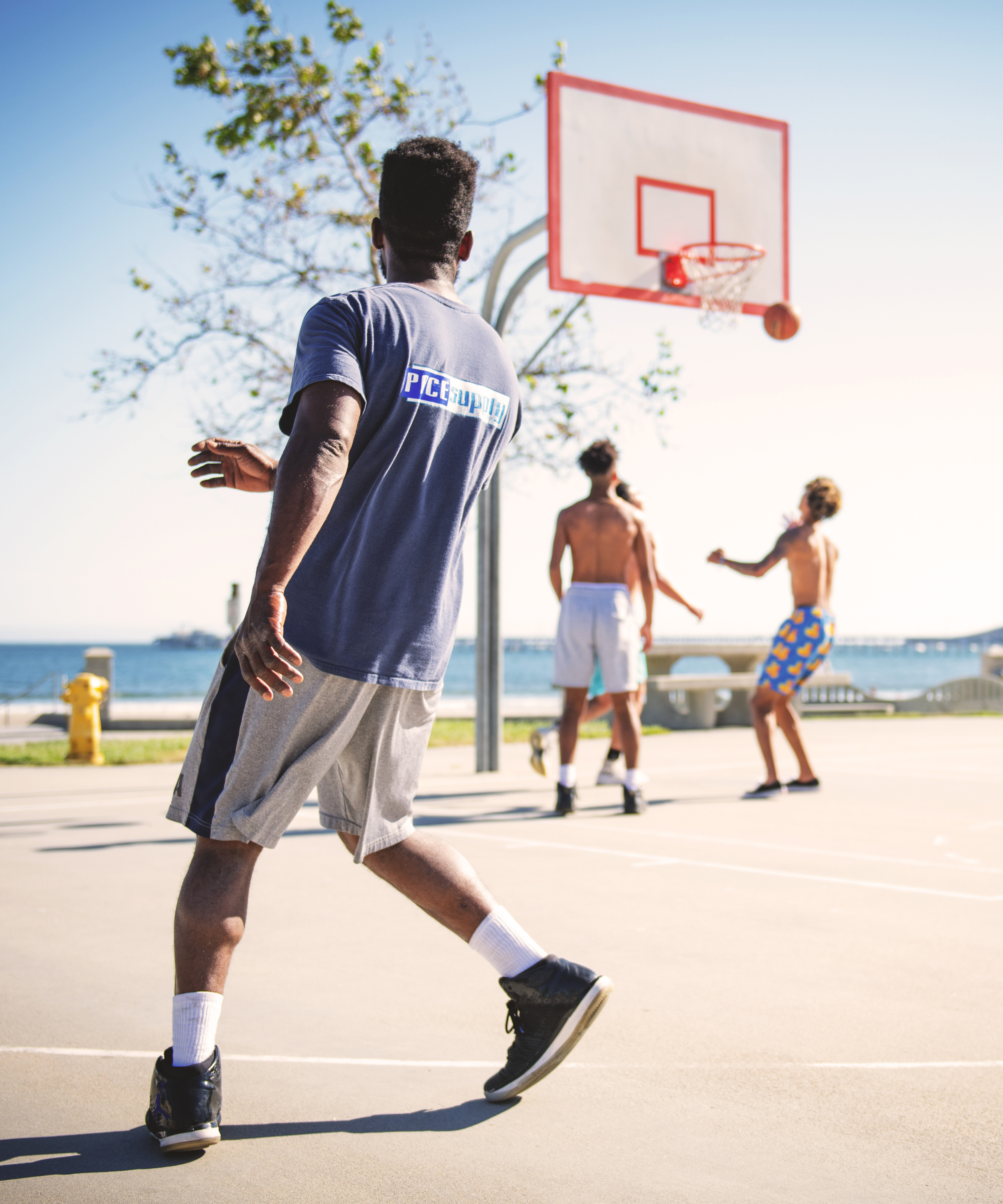 Person playing basketball on an outdoor court with a clear sky and trees in the background.