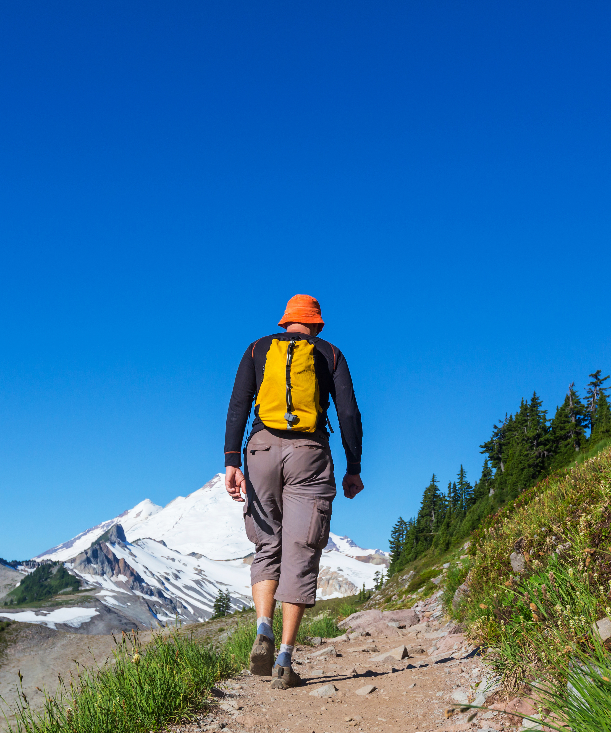 Person hiking on a mountain trail with a clear blue sky