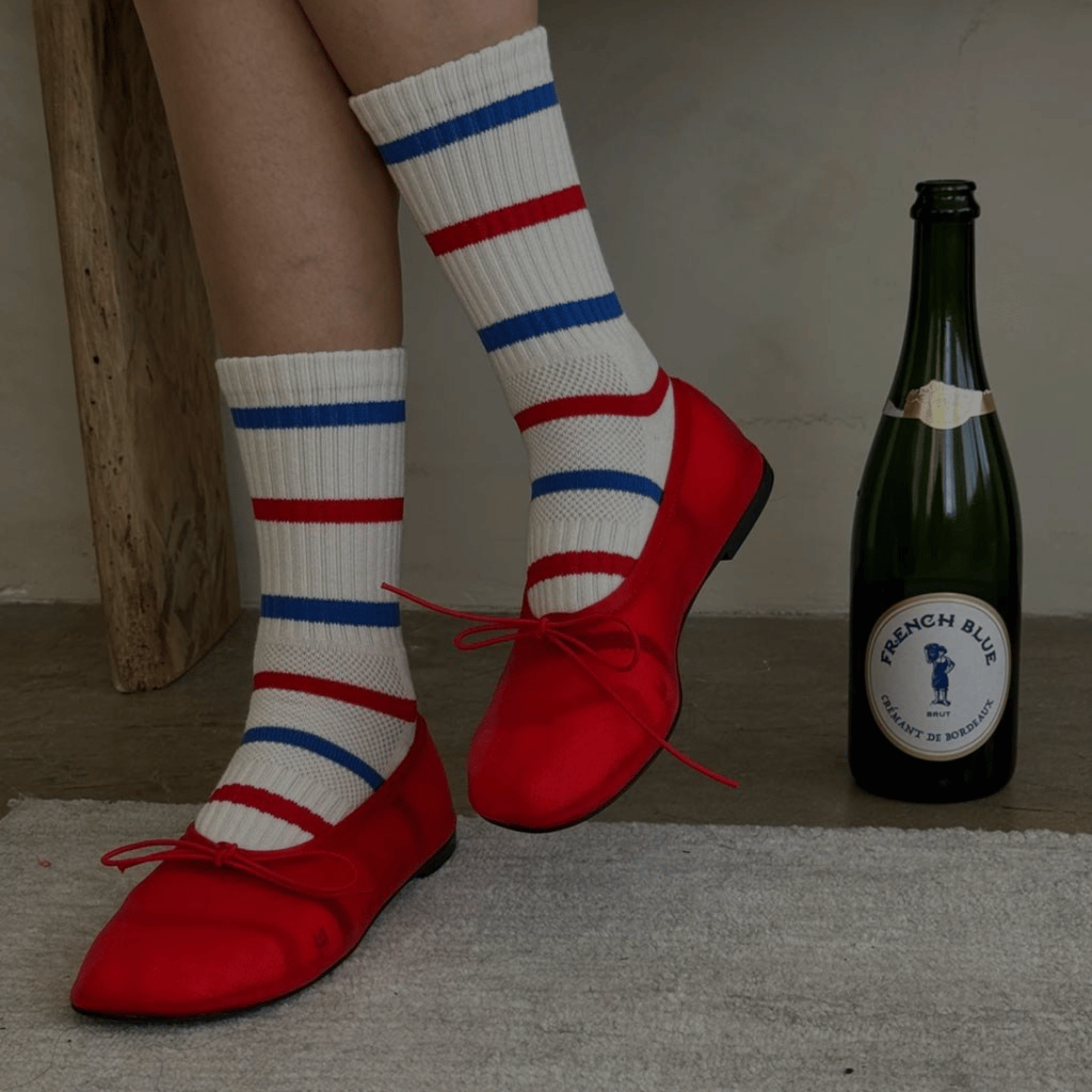 Person wearing red shoes and striped socks next to a bottle of champagne.