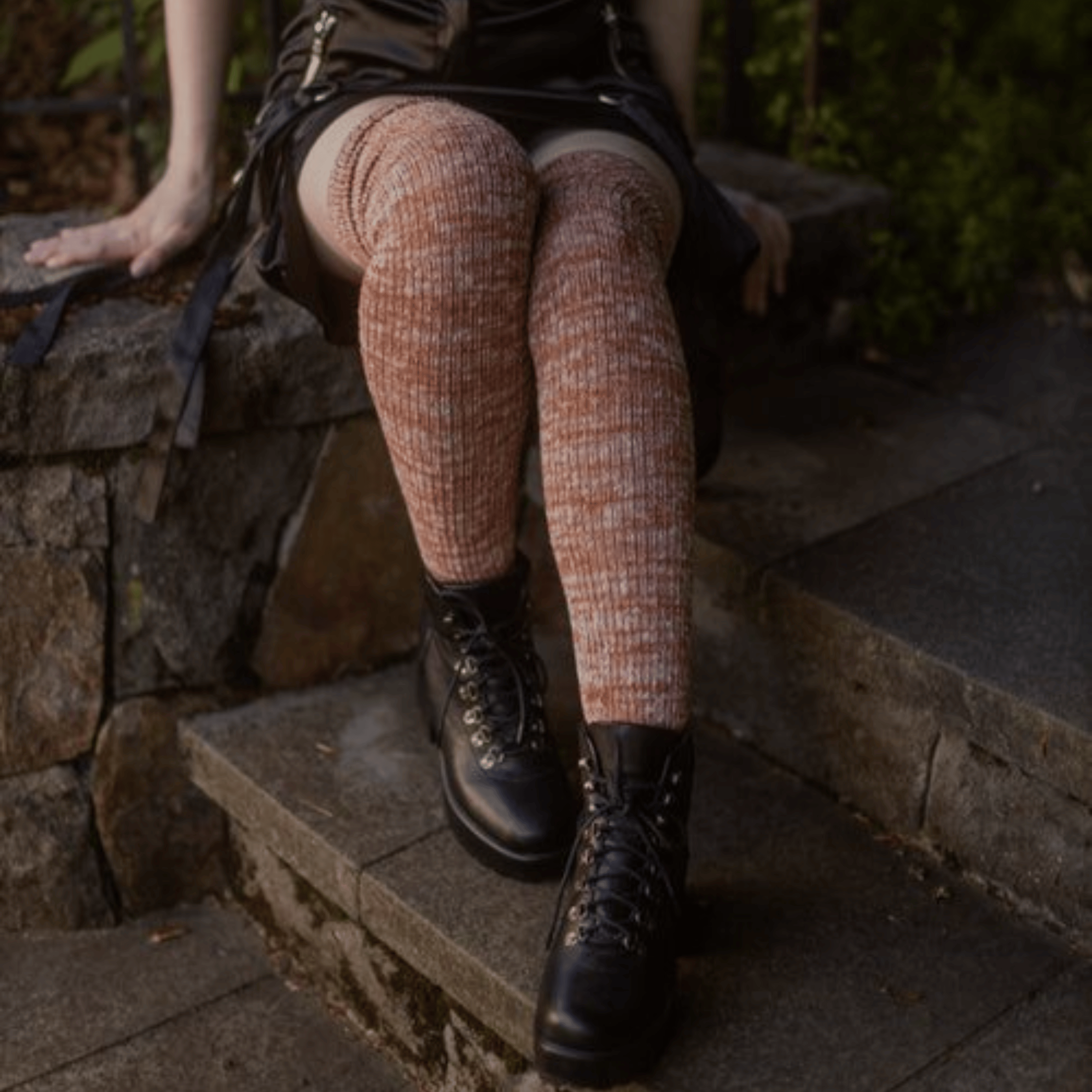 Person wearing checkered leggings and black boots sitting on stone steps.