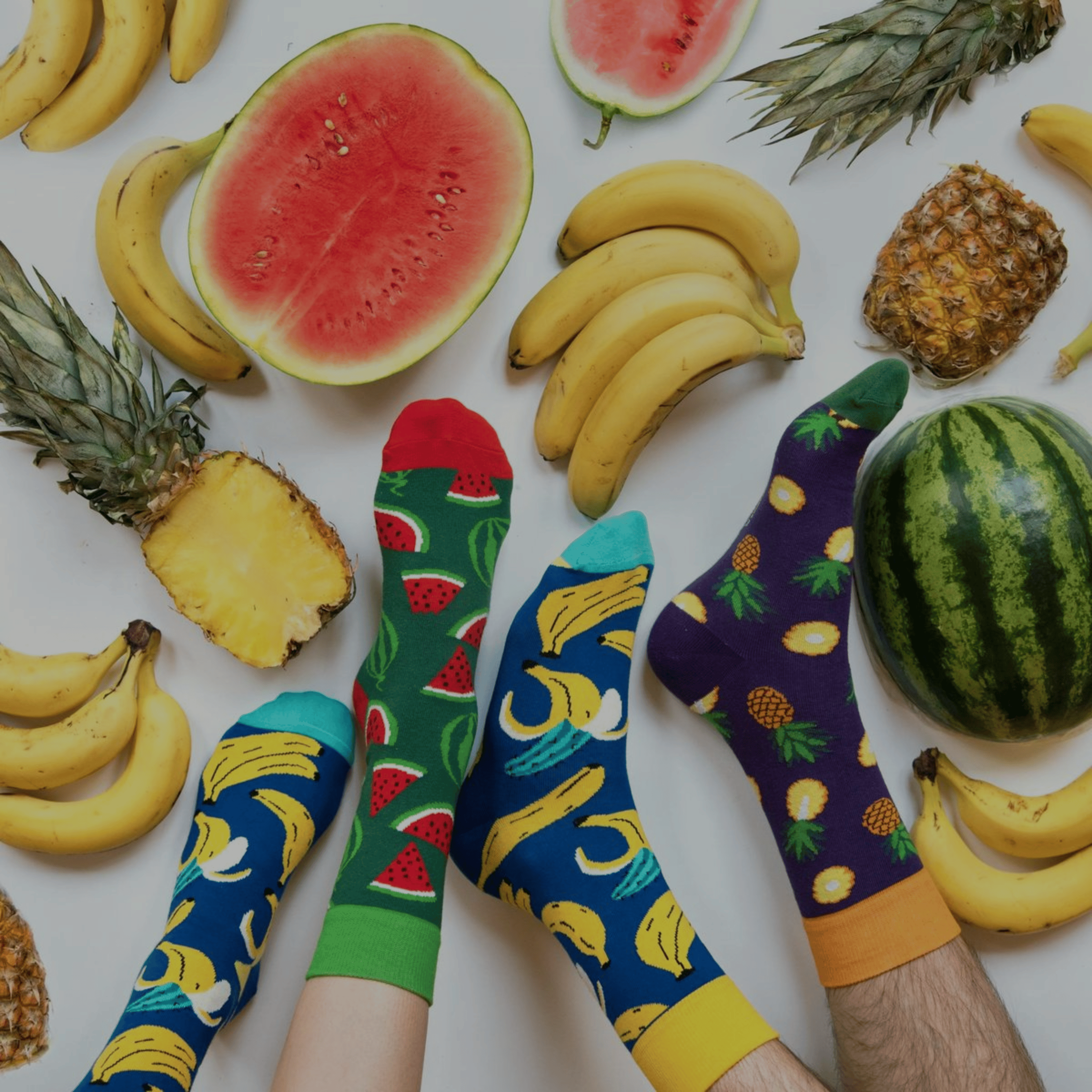 Colorful socks with fruit patterns on a background of fruits including watermelons, bananas, and pineapples.
