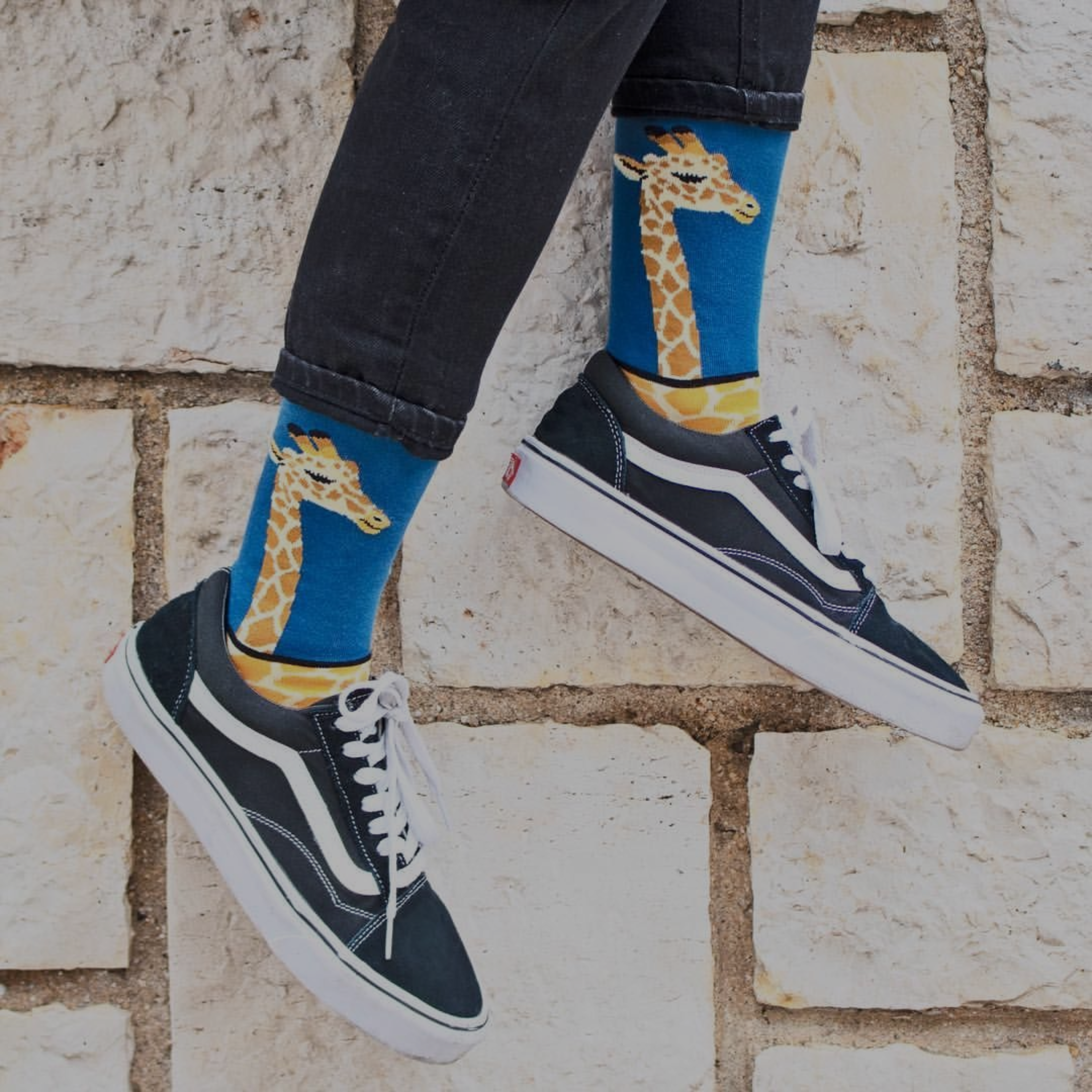Person wearing blue socks with giraffe design and black sneakers on a stone floor.