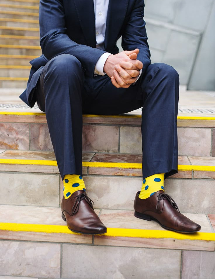 Person wearing a navy suit with yellow polka dot socks sitting on steps.