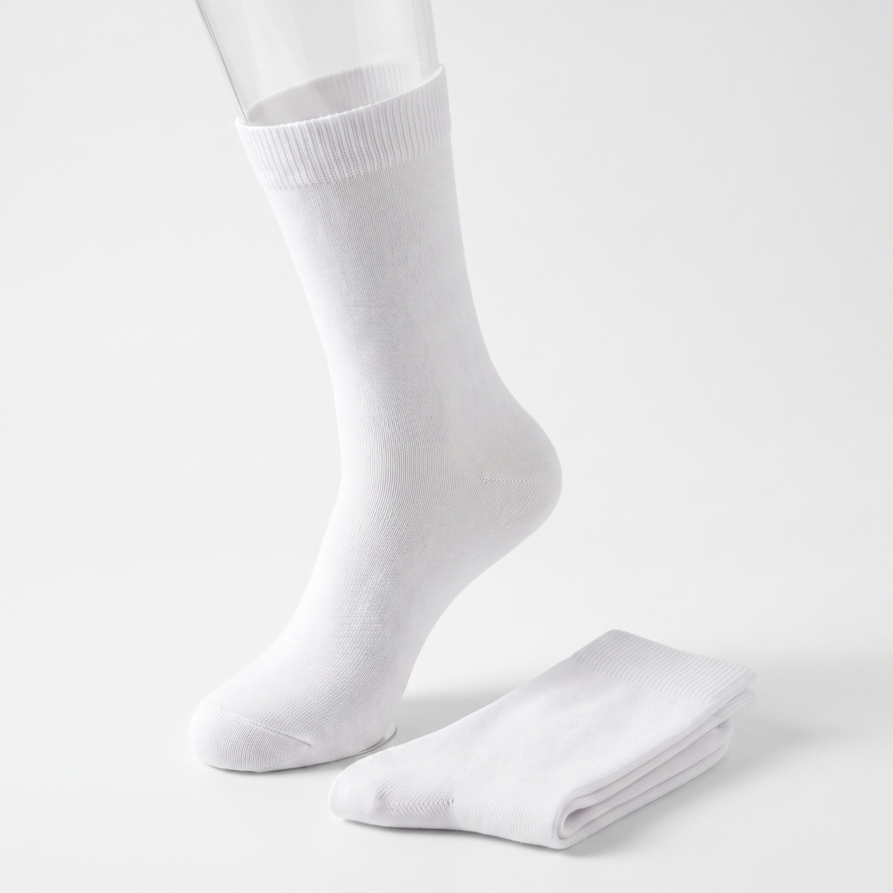 A pair of plain white crew socks, with one sock displayed on a clear mannequin foot and the other folded neatly beside it, set against a seamless white studio background.