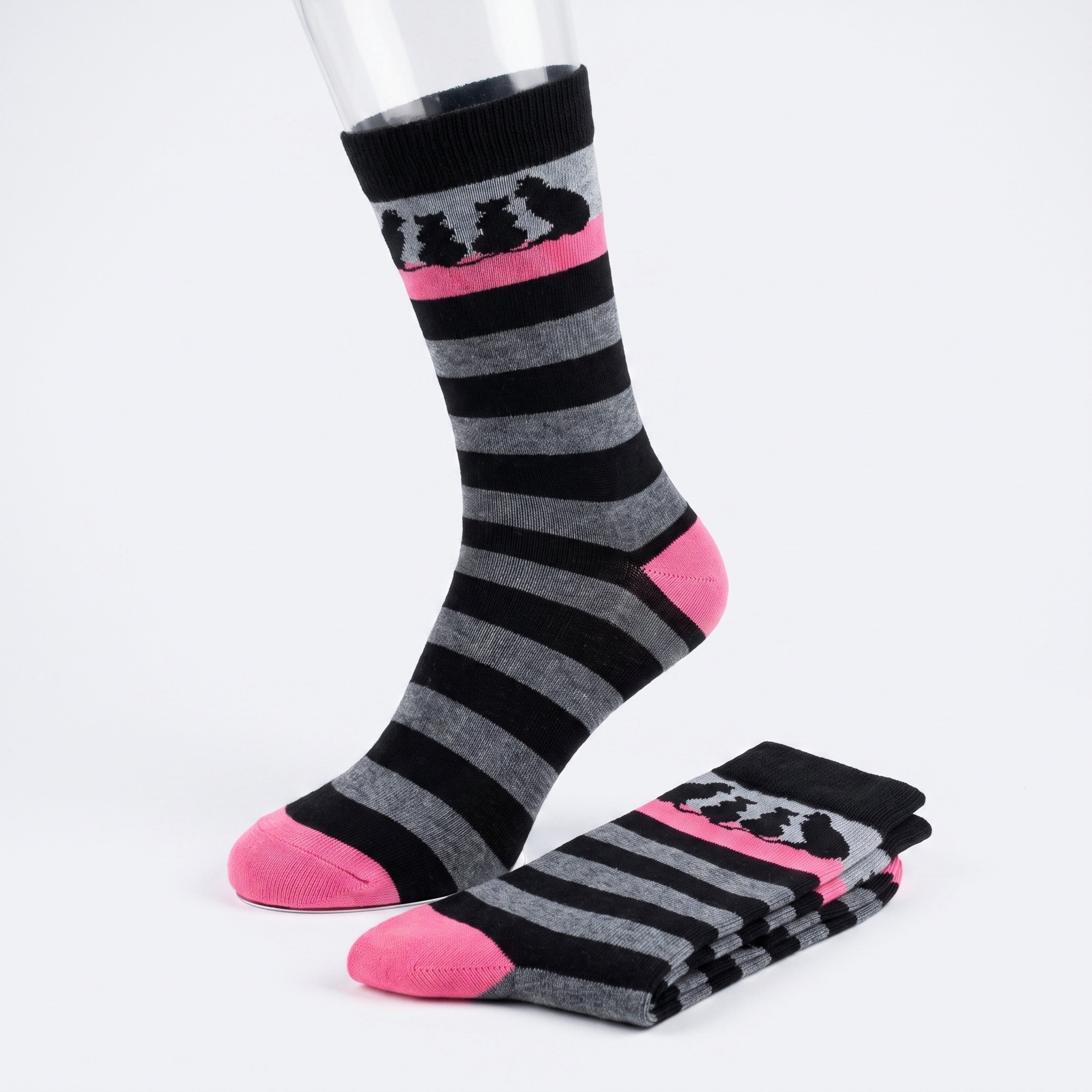 A pair of crew socks with black and gray horizontal stripes, featuring a pink band near the cuff with black cat silhouettes and bright pink toes and heels. One sock is displayed on a clear mannequin leg, while the other is folded on a white studio background.