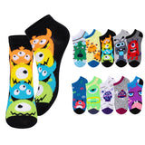 A set of colorful low-cut ankle socks with cartoon monster prints, shown on a white background. The main pair on the left is black with stacked orange, yellow, blue, and green monsters.